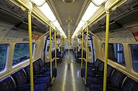 View down the interior of London Underground 1995 stock train in January 2014, with yellow-speckled dark grey flooring, dark blue patterned seats and vertical yellow hand rails