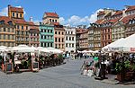 Market square, colourful houses in the background, tourists in restaurants in front