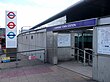 A grey building with a black top and a blue sign reading "CANNING TOWN STATION" in white letters all under a blue sky with white clouds