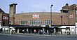 A brown-bricked building with a rectangular, dark blue sign reading "WOOD GREEN STATION" in white letters all under a light blue sky