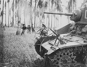 ngày 7 tháng 1 năm 1943. Australian forces attack Japanese positions near Buna. Members of the 2/12th Infantry Battalion advance as Stuart tanks from the 2/6th Armoured Regiment attack Japanese pillboxes. An upward-firing machine gun on the tank sprays treetops to clear them of snipers. (Photographer: George Silk).