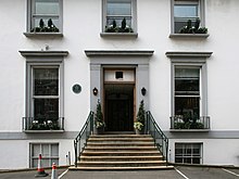 A two storey white building with grey window frames, several cars are parked in the foreground.