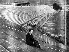 Black and white photo of the stands in a stadium with someone sitting on one