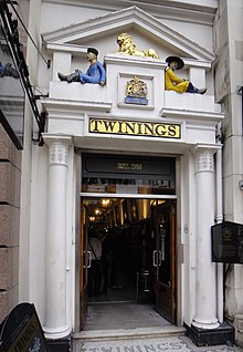 A door with white columns and a pediment. A painted figure sits on either side of the pediment, and the name "Twinings" is spelled out in gold over the door.
