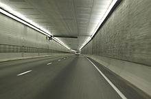 A two-lane freeway without any safety lanes or shoulders is proceeding down a lighted square passageway.