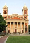 Ground-level view of church with an orange facade and a large portico; two twin bell towers extend from both sides of the building.