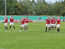 Eight F.C. United players at the edge of the penalty box after a game. Six of the players are clapping the fans.