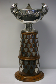 Sterling silver bowl with gold trim and three handles in the shape of leopards atop of a wooden plinth