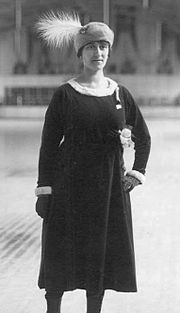 Photographie montrant Magda Julin debout en robe foncée et portant un bonnet à plume.