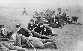 Photographie d'une unité d'infanterie pendant un exercice. Aux côtés des soldats, des infirmières sont visibles.