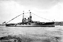 A large gray battleship sits in harbor