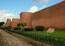 Photo en couleur montrant des fortifications de couleur ocre, au premier plan une route en pavé et des jardins.