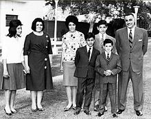 A group of related people posing outdoors. From left to right, there are three women dressed in shirts and long skirts, three boys dressed in suits and ties and a man in a suit and tie