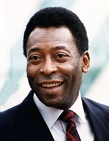 Farbiges Portraitfoto von einem lächelnden Mann, der einen dunklen Anzug und eine rot-schwarze Krawatte trägt.