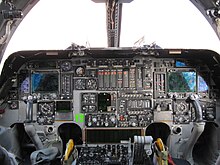 A flightdeck, dominated by a mix of new and analogue instruments. On both sides are control yokes. Light enters through the forward windows