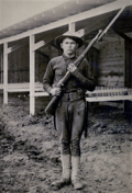 A black and white image of a young soldier holding a Model 1903 Springfield Rifle in front of a stable
