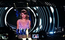 A young woman performing onstage while the screen behind her focuses on her face