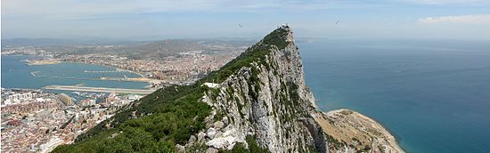 À l'avant-plan le Rocher, avec à l'est des falaises subverticales et à l'ouest des pelouses moins inclinées ; au fond, la presqu'île