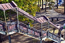 A staircase from the sidewalk to the elevated station house. It has decorative railings with peeling black paint.