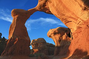 Metate Arch, a slender natural rock arch with a reddish-brown hue at sunset