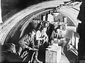 Interior of a dugout occupied by officers of the 105th Howitzer battery of the 4th Brigade. Three officers are looking at papers in the light of two candles on an upturned box