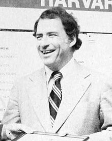 Bob Kiley in a suit in front of a Harvard MBTA station sign