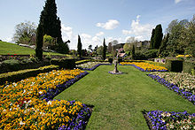 Formal garden with trimmed lawn, flower beds and stone plinth under a clear sky