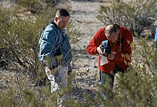 Photographie en couleur d'Armstrong et d'Aldrin photographiant le sol lors d'une formation dans une zone aride.