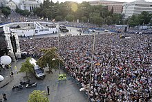 Vantage photograph of a fenced crowd in white jerseys. Some areas are void of people.