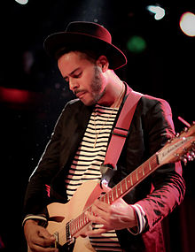 A picture of George "Twin Shadow" Lewis Jr., a man in his late 20s, playing the guitar.