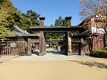 The main entrance to the park. There is a gate made of wood in the center, with wooden structures on both sides.