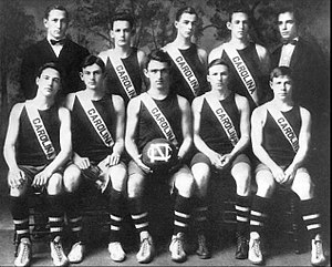 Five young men in American basketball uniform seated with one holding a basketball with the North Carolina insigna, and five men standing behind them, two older men in jackets with bow ties and three young men in American basketball uniform