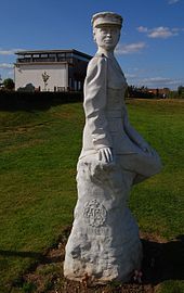 "White statue of a woman in uniform, with a chapel in the background."