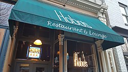 Photograph of an entrance to a building with "Hobo's Restaurant and Lounge" printed on a green covering; in the window is a sign for video lottery