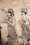 two women in fine dress play harps