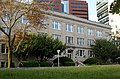 An office building made of light brick with large colonial-style windows stands in front of taller, more modern looking office buildings.