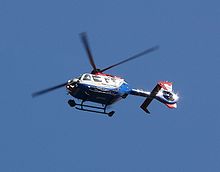 A blue and white painted helicopter flying in blue sky, pictured from below.