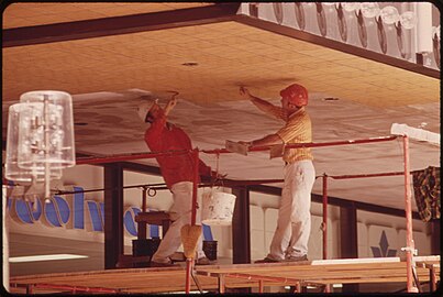 Photographie des années 1970 montrant deux ouvriers sur échafaudage en train de poser le carrelage en sous-face d'une passerelle.