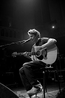 Howard playing an acoustic guitar while singing into a microphone onstage