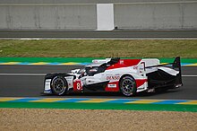 A side photograph of a white, red and black Le Mans Prototype 1 racing car with the number 8 in a red square painted near the front-left wheel