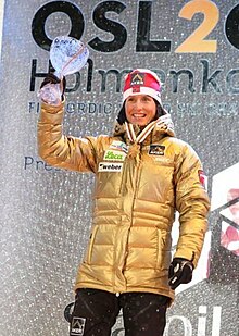 Skieuse sur un podium, levant une coupe en verre de la main droite.