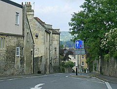 Street scene with yellow stone houses on the left and trees showing above a wall on the right