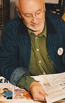 Photographie d'un homme portant des lunettes et lisant des documents étalés devant lui.