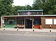 A red-bricked building with a rectangular, dark blue sign reading "MOOR PARK" in white letters and four black-striped posts in front