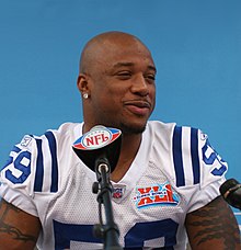 African American male in football uniform seated at a press conference with Super Bowl XLI logo in the background and an NFL logo on the microphone