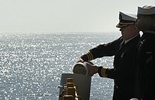 Photographie en couleur d'un homme en uniforme dispersant les cendres de Schirra depuis un navire.