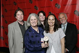 A group of 5 people smiling in a photograph against a red backdrop.