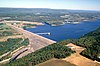 An aerial view of a large dam and lake surrounded by forest with low mountains in the background