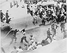 group of men holding pipes confronting police on street seen from above