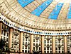 Interior of a domed atrium surrounded by hotel rooms and tall columns with light coming in through blue windows